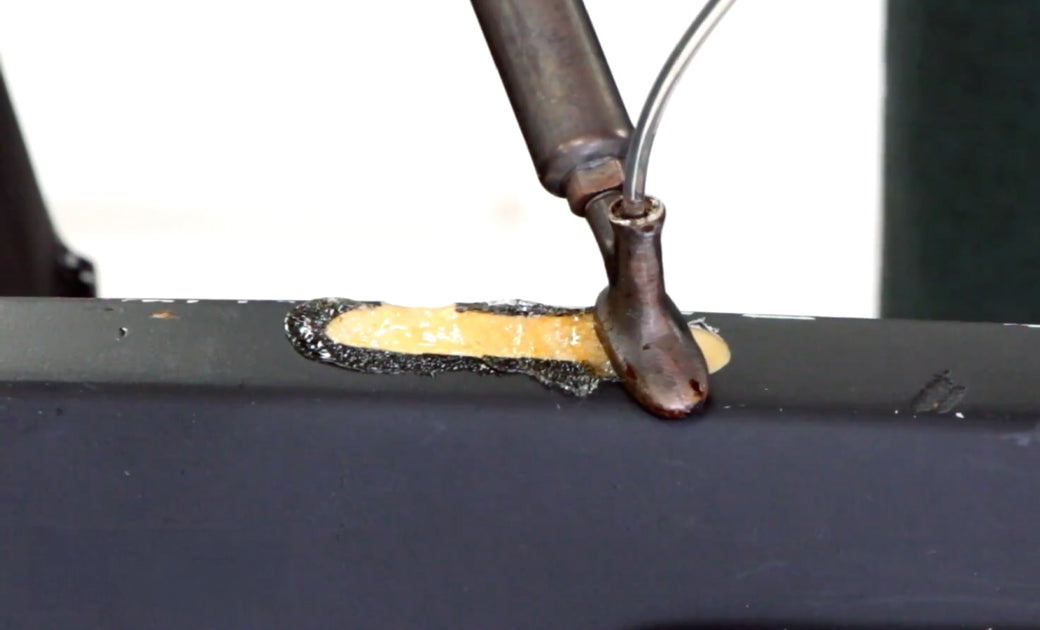 A urethane bumper cover with a crack is being repaired by an airless plastic welder. PUR rod is being fed through the tube in the airless welder tip.