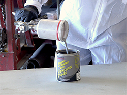 A man pouring paint out of a paint gun and into a can.