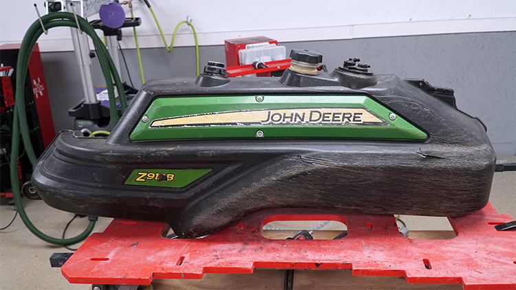 A black gas tank for a John Deere zero turn mower.