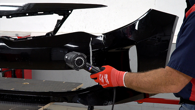 A person using a heat gun to heat the frontside of the bumper cover.