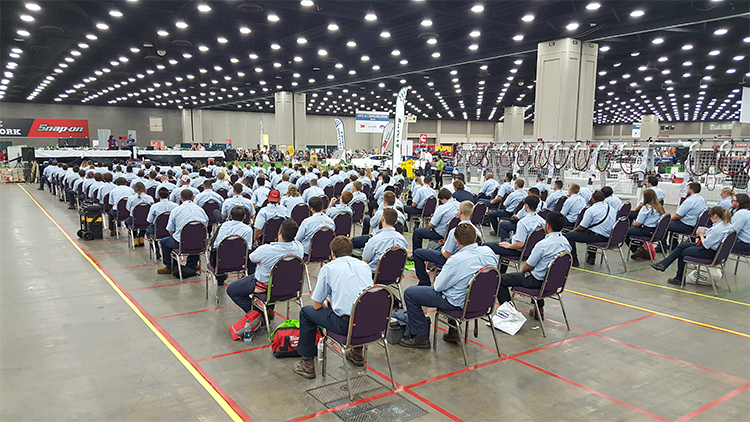 The competitors seated in chairs listening to a speaker.