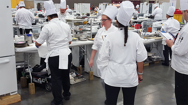 Competitors standing around dressed in chef's attire.